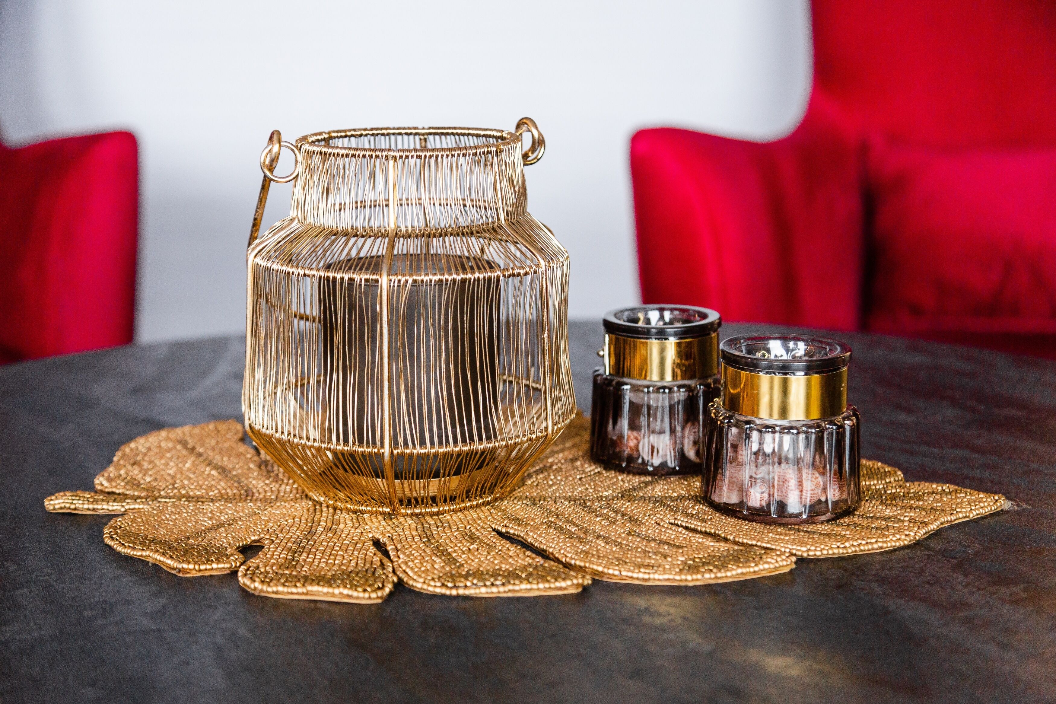 A decorative glass container with handles, two smaller glass containers, and a woven placemat on a table.