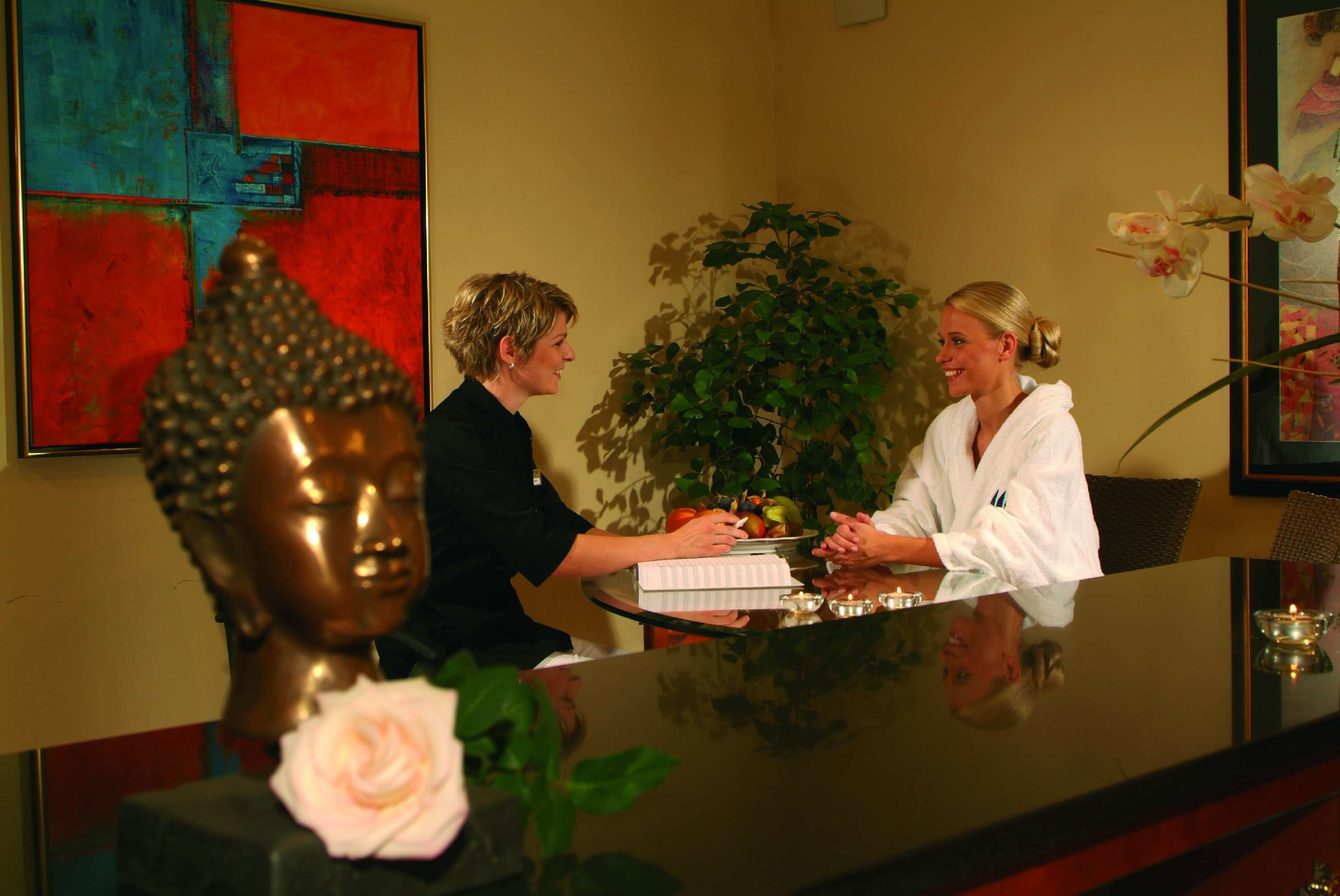 Un área de recepción con una estatua de Buda, un jarrón con una flor rosa y un cuadro abstracto grande en la pared.