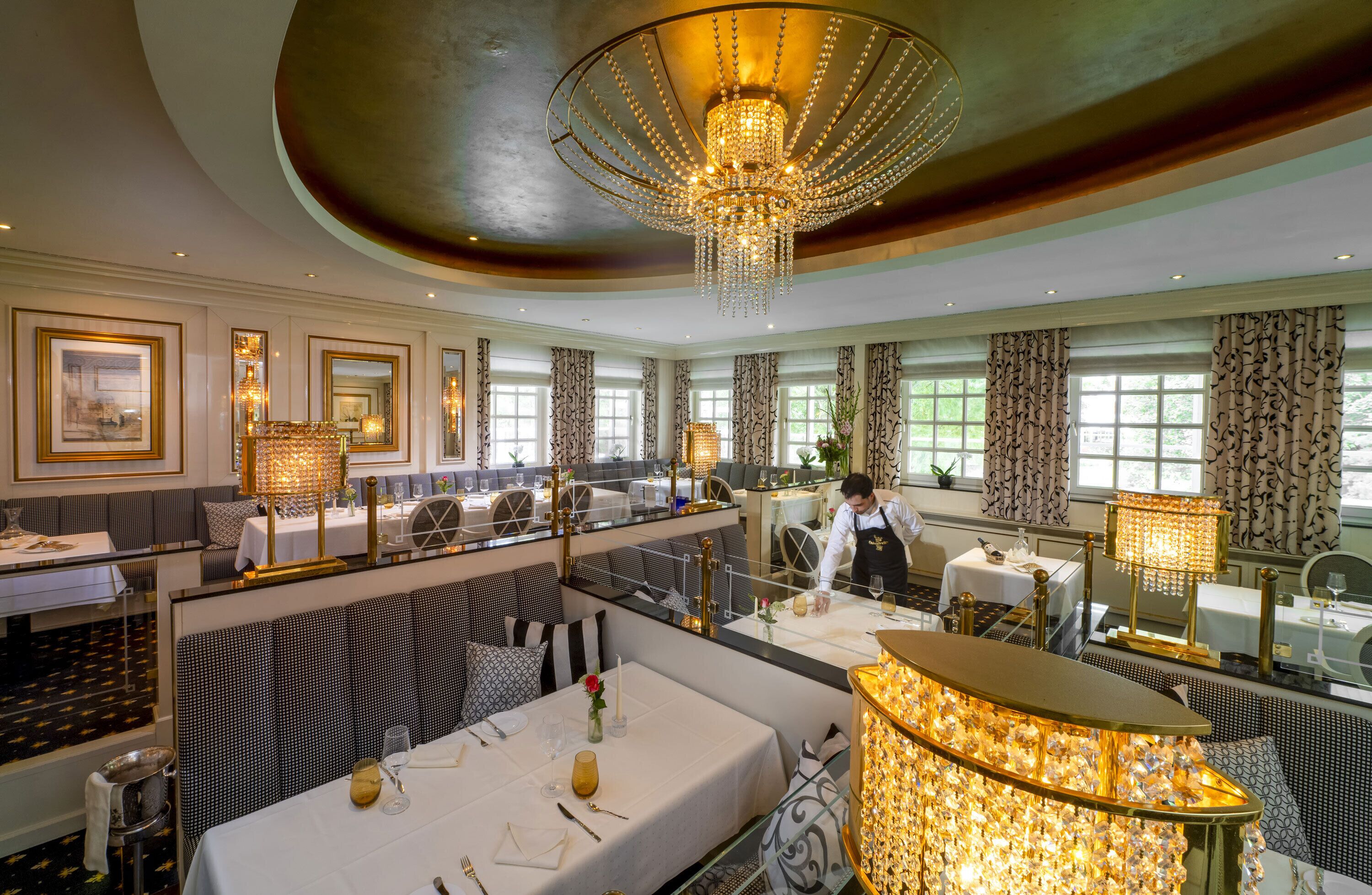 Een luxueuze eetruimte met meerdere tafels, elegante kroonluchters en decoratieve gordijnen.