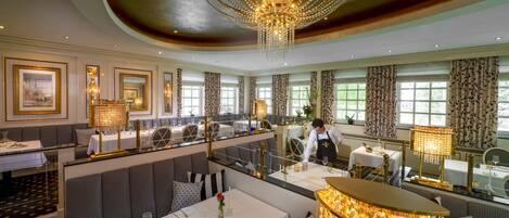 Een luxueuze eetruimte met meerdere tafels, elegante kroonluchters en decoratieve gordijnen.