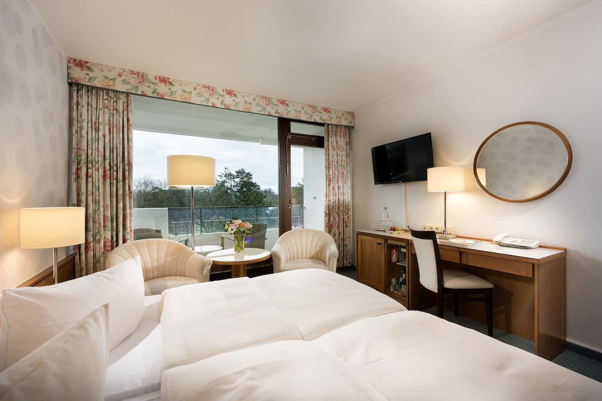 Ein Hotelzimmer mit einem großen Bett, einem Schreibtisch mit Stuhl, einem Fernseher und einem Fenster mit Vorhängen.