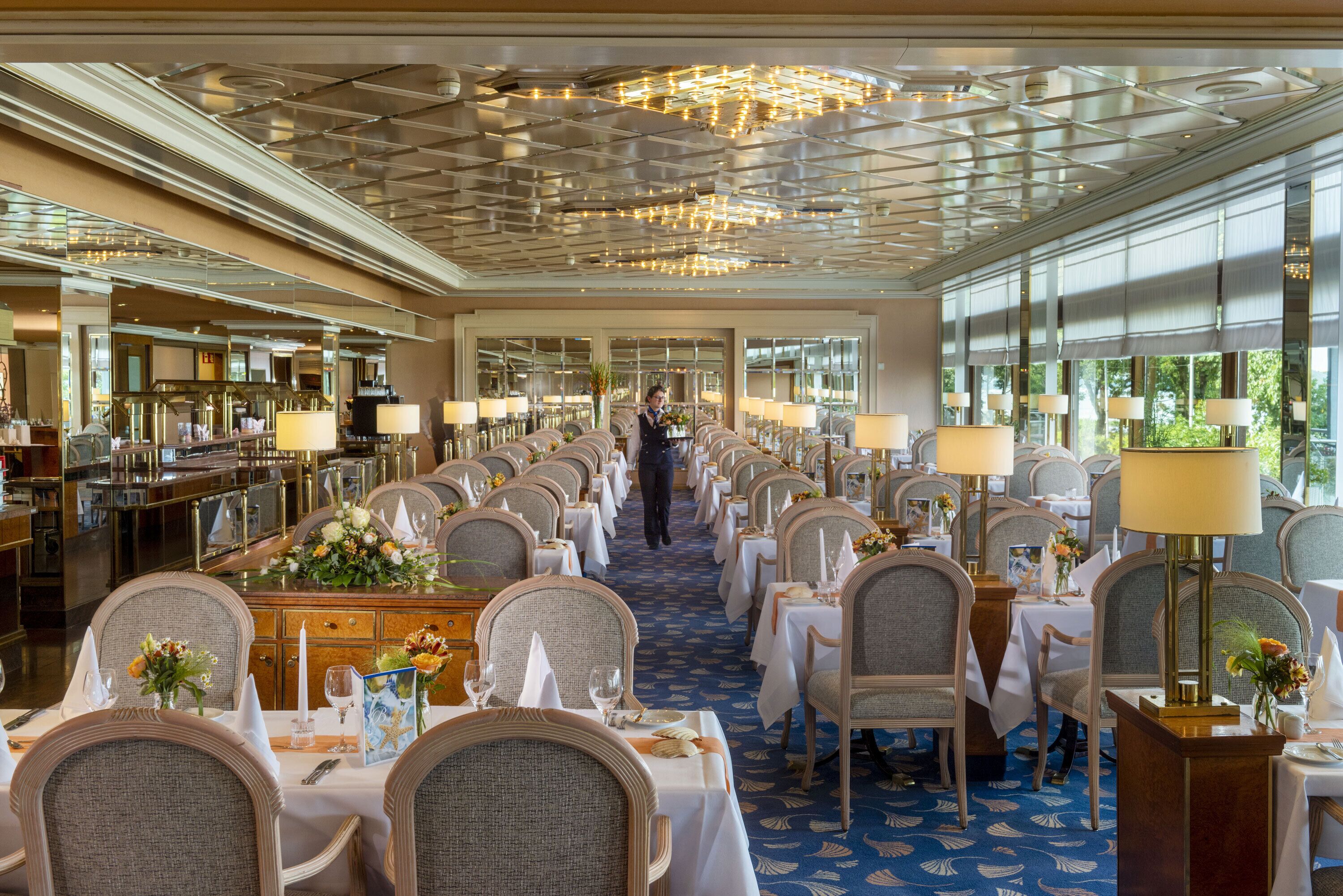 A hotel dining area with long tables, chairs, and chandeliers.