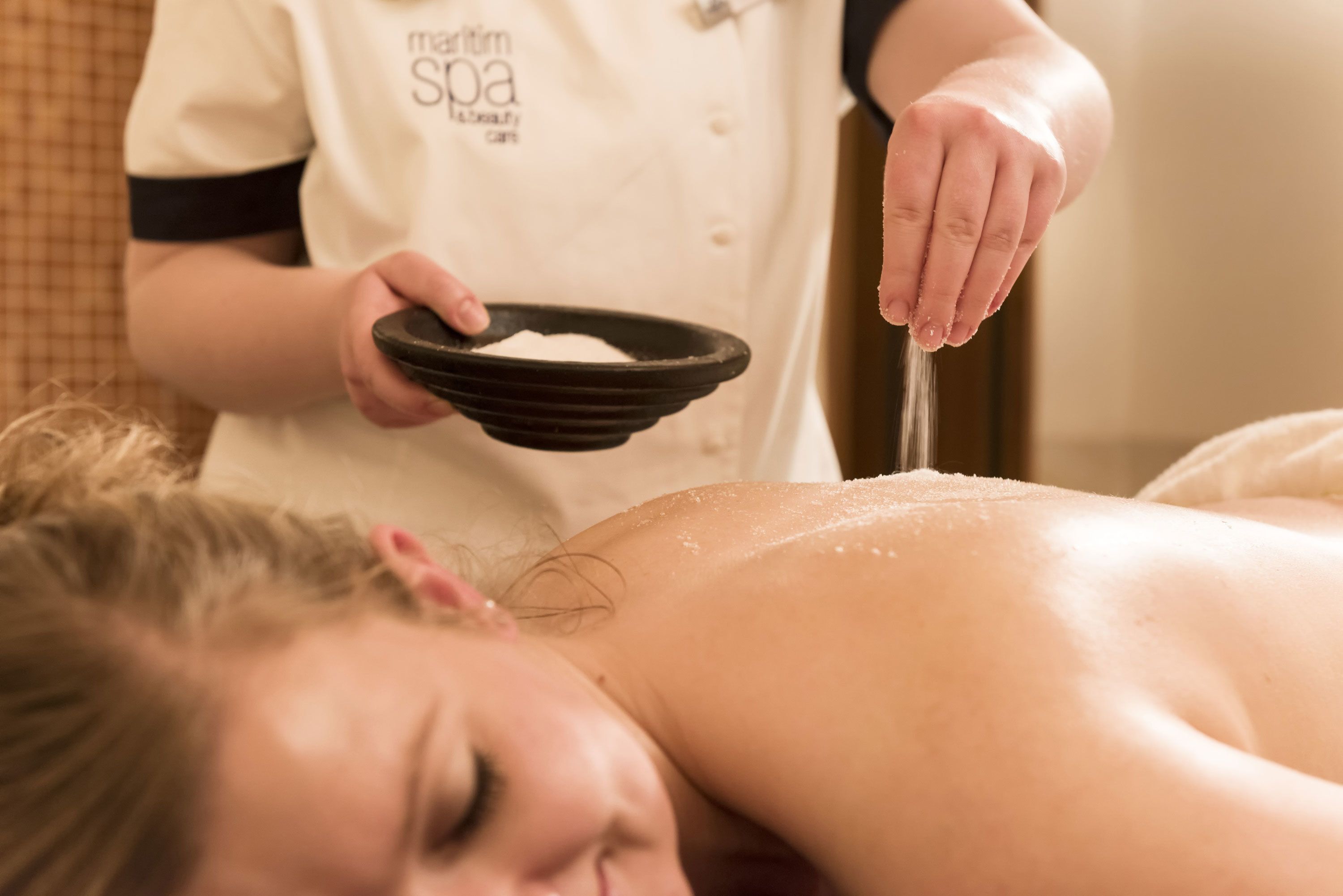 A person receiving a facial treatment, with a bowl of powder and a brush.