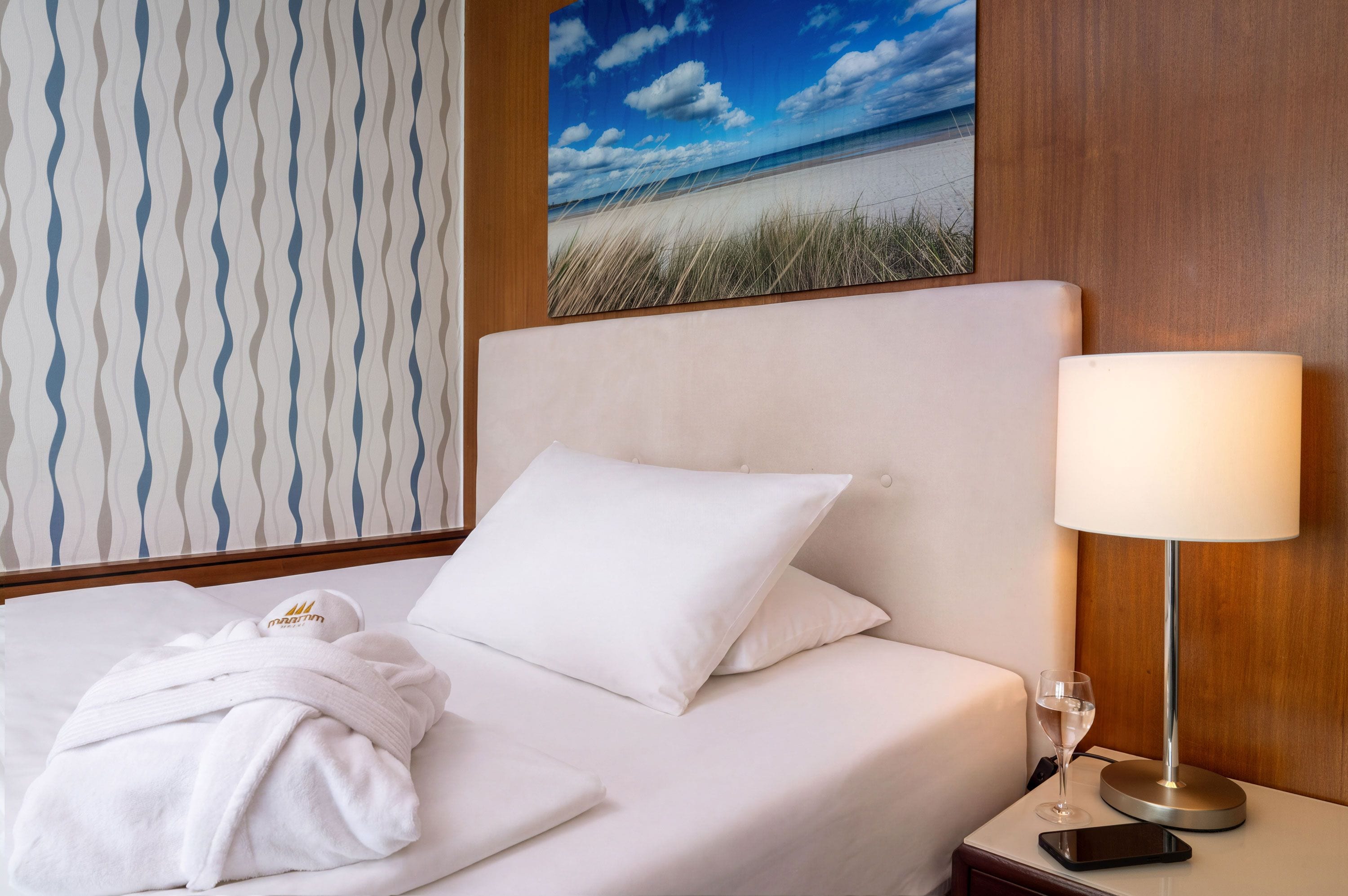 Habitación de hotel con una cama, una lámpara de noche, un vaso de agua y un teléfono inteligente en la mesita de noche.