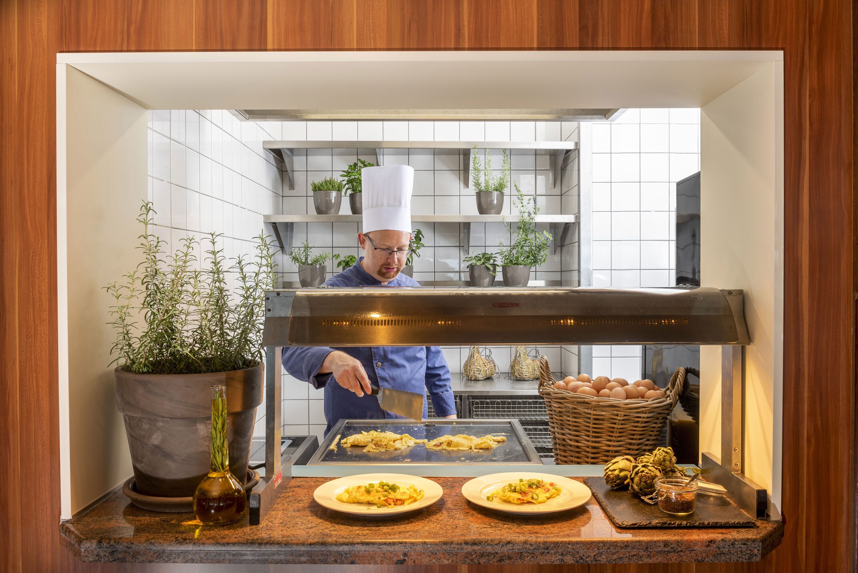 A chef preparing food in a kitchen with a counter, potted plants, and a basket of eggs.