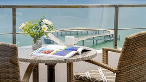 A balcony with wicker chairs, a table with a magazine, a vase with flowers, and a view of the sea and a pier. - Maritim Seehotel Timmendorfer Strand (Timmendorfer Strand)