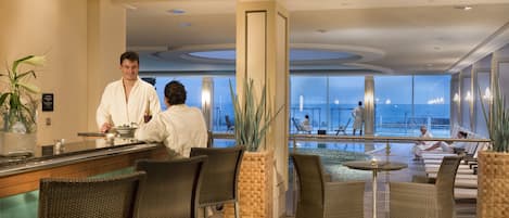A hotel lobby with a bar area, seating, and a pool view.