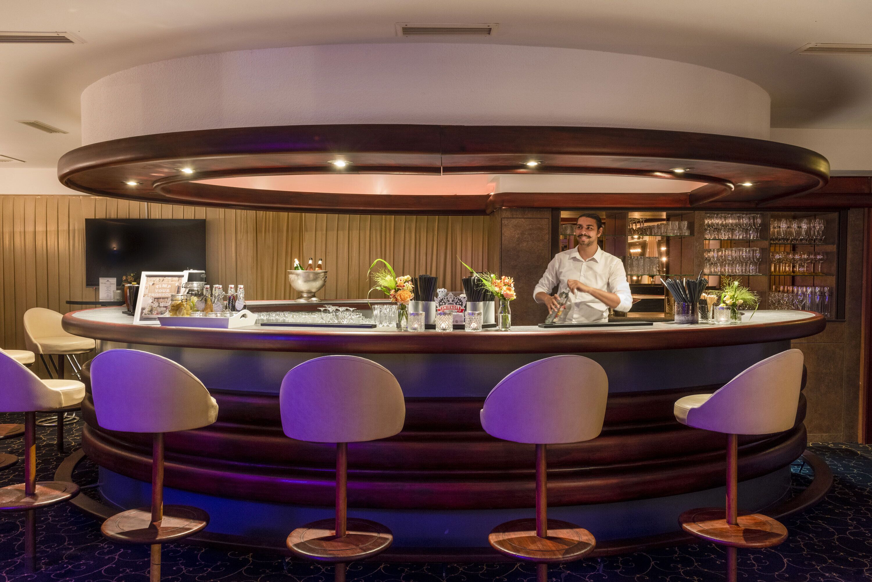 A bar area with a circular counter, bar stools, and a bartender.