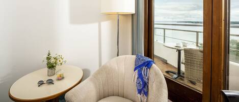 A corner room with a round table, a lamp, a chair, and a view of the outdoors.
