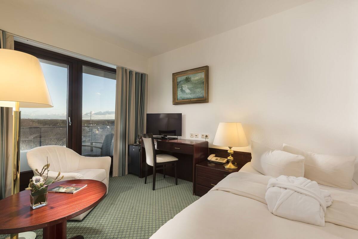 Ein Hotelzimmer mit Bett, Schreibtisch, Stuhl, Fernseher und einem Fenster mit Vorhängen.