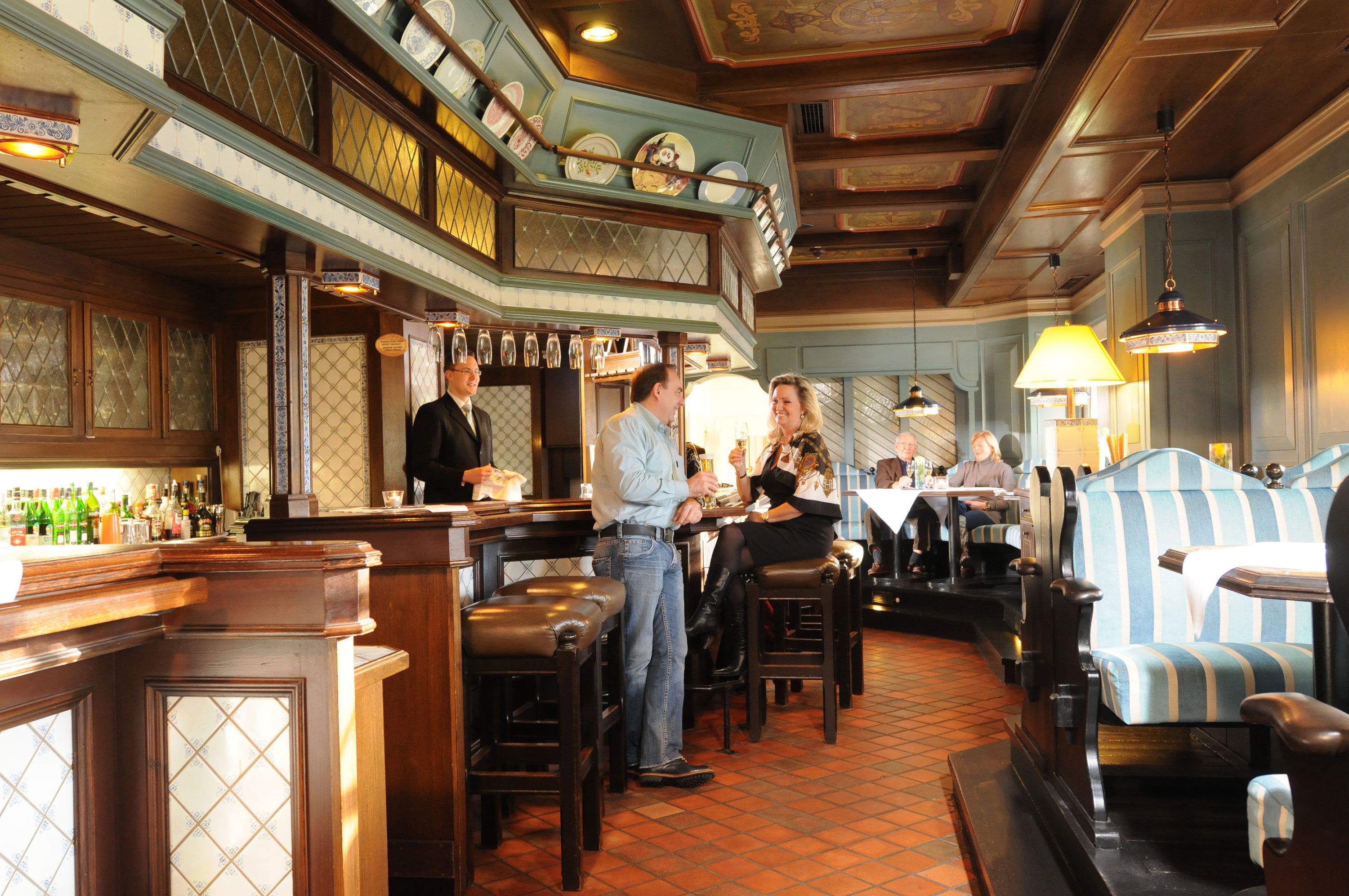 A bar area with wooden furnishings, a tiled floor, and a variety of bottles on the shelves.