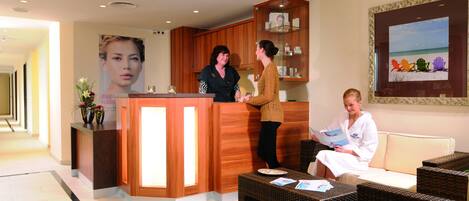A reception area with a wooden reception desk, a seating area with wicker furniture, and a framed beach scene on the wall.