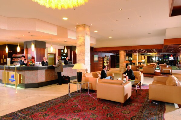 A hotel lobby with a reception desk, seating area, and a large chandelier. - Maritim Strandhotel Travemünde (Lübeck)