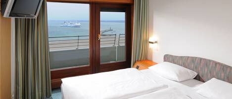 Habitación de hotel con dos camas, televisión y vista al mar y un barco.