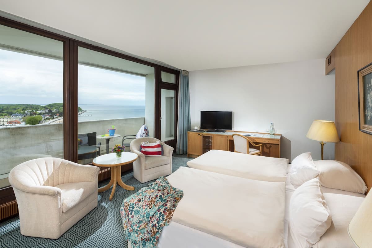 A hotel room with a balcony, a bed, a sofa, a desk with a TV, and a lamp.