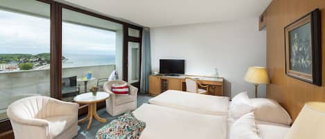 Habitación de hotel con balcón, una cama, un sofá, un escritorio con televisor y una lámpara.