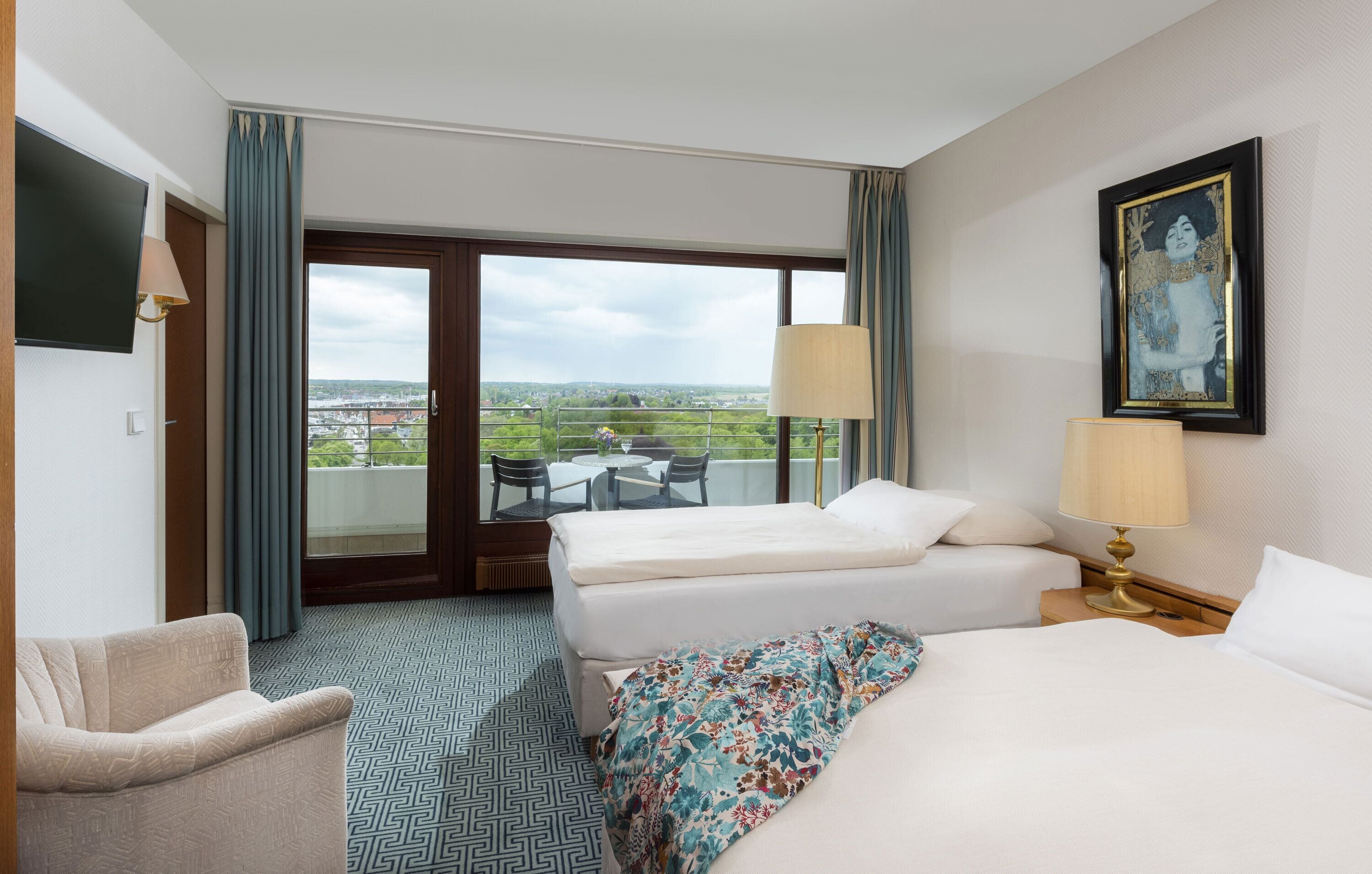 Une chambre d’hôtel avec deux lits, un canapé, une télévision, un balcon avec vue et un tableau au mur.