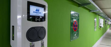 A modern hotel corridor with a green wall, an electronic payment kiosk, and a sign indicating an E-Zone parking area.