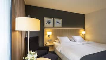 A hotel room with a bed, two bedside tables, a desk with a chair, a lamp, and two framed pictures on the wall.