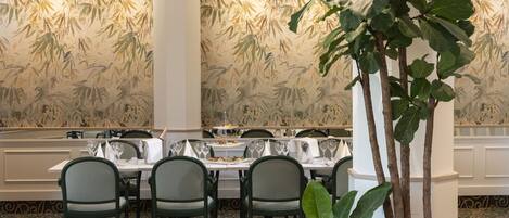 A dining area with tables set for a meal, chairs, and a large potted plant.