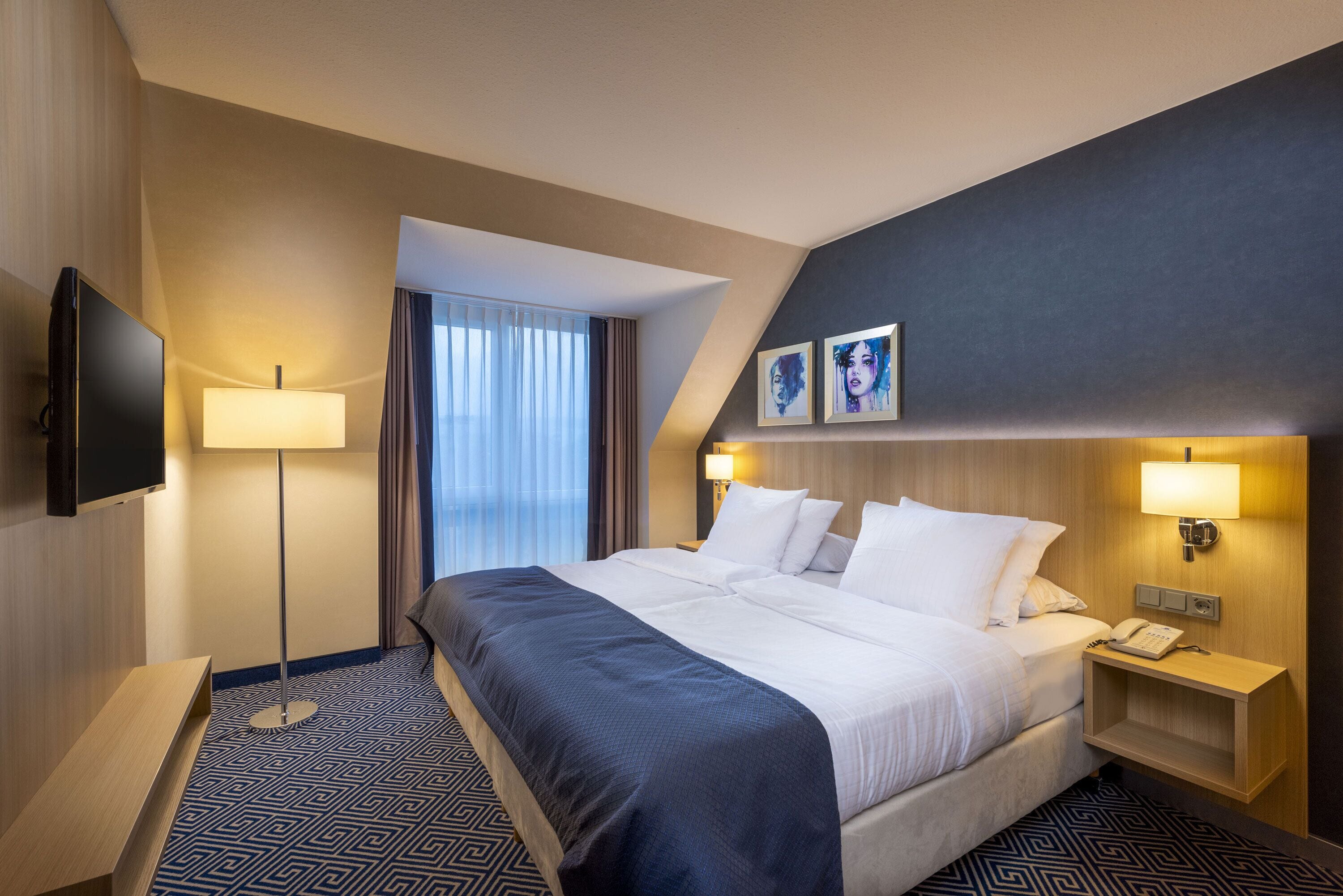 A hotel room with a large bed, a flat-screen TV, a bedside table, and a lamp.