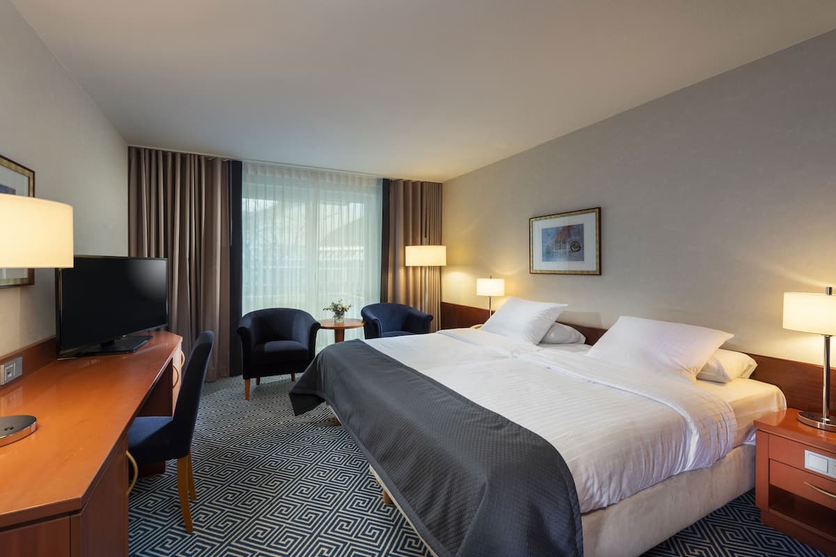 Ein Hotelzimmer mit einem Bett, zwei Sesseln, einem Schreibtisch, einem Fernseher und Lampen.