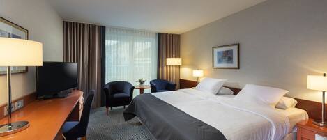 Una habitación de hotel con una cama, dos sillas, un escritorio, un televisor y lámparas.