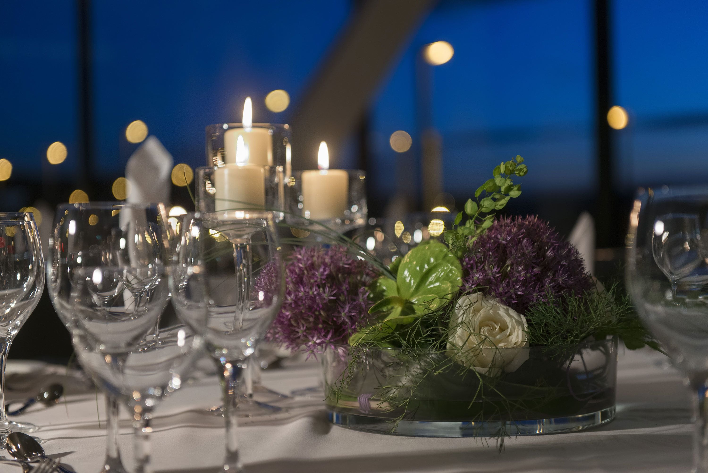 Ein Tisch ist gedeckt mit Weingläsern, Kerzen und einer Blumendekoration.