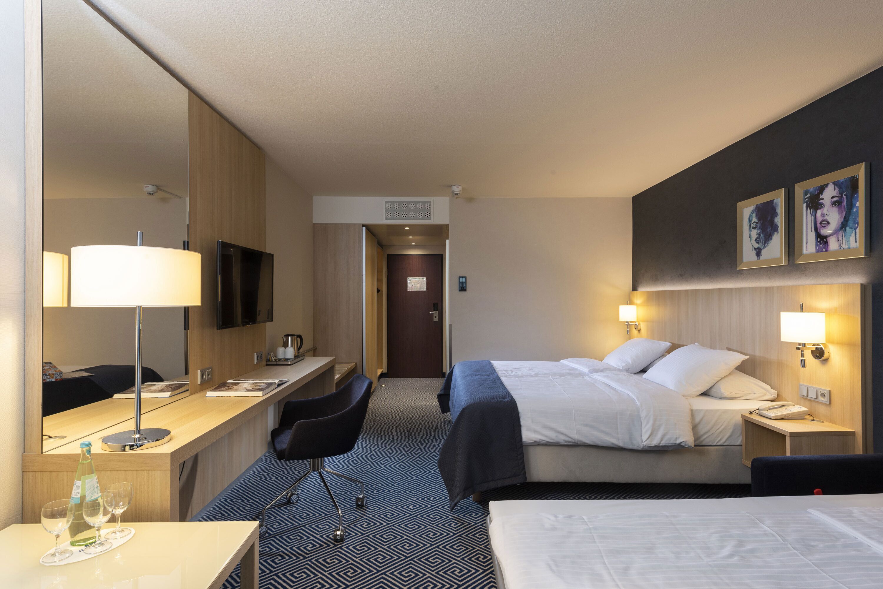Une chambre d’hôtel comprenant un lit, une table de chevet, une lampe, un bureau, une chaise et un téléviseur.