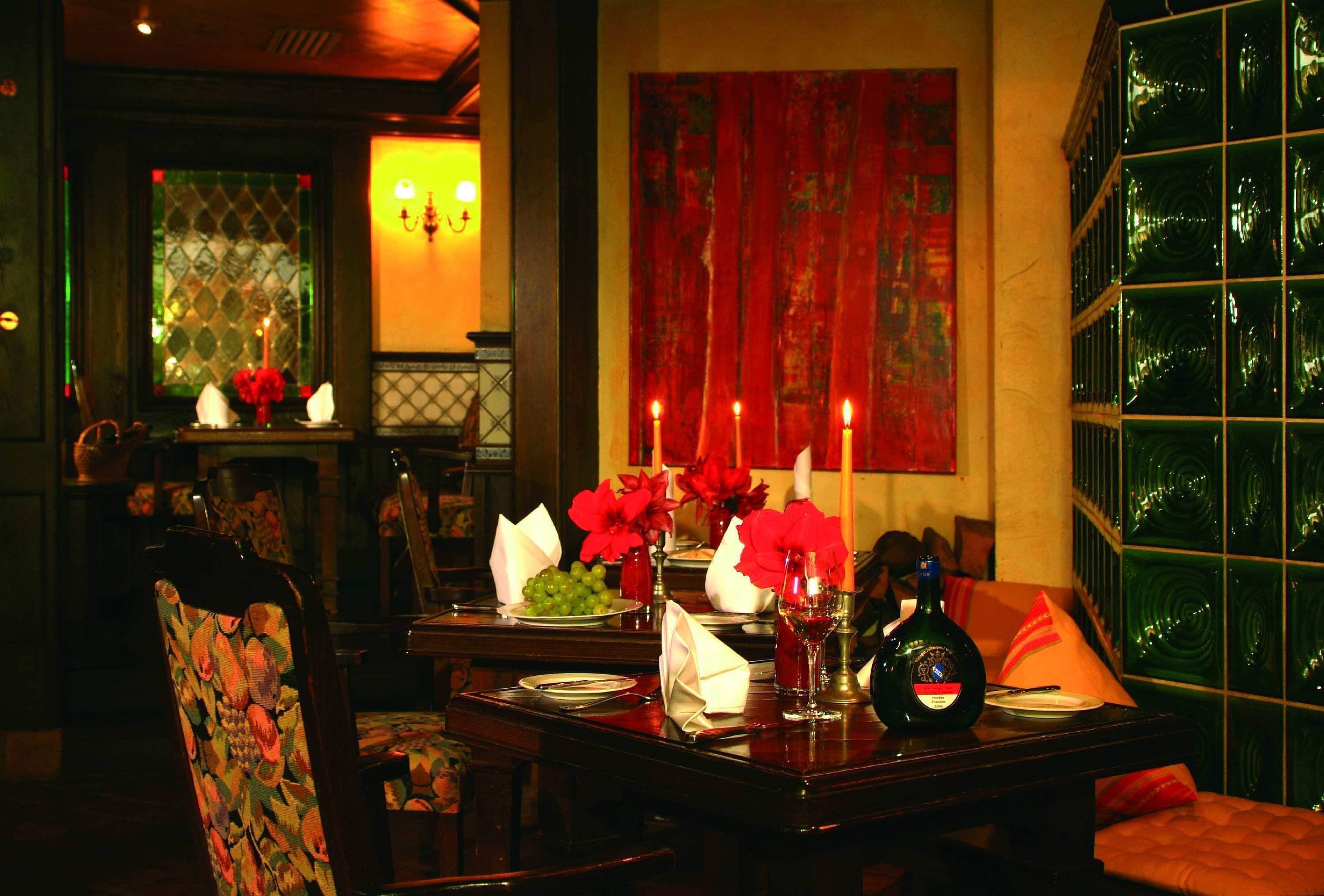 A dimly lit dining area with a table set for two, featuring a bottle of wine, glasses, and a vase of red flowers.