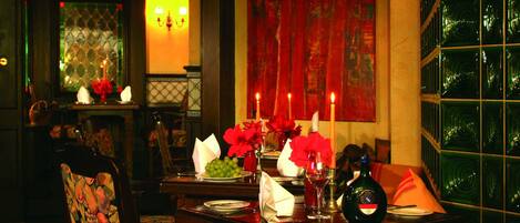 A dimly lit dining area with a table set for two, featuring a bottle of wine, glasses, and a vase of red flowers.