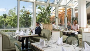 A restaurant with a glass ceiling, green upholstered seating, and a view of trees and buildings outside. - Maritim Hotel Würzburg (Würzburg)