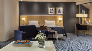 Una habitación de hotel con una cama, dos sillas, un escritorio y una mesa de centro. Hay un libro y un jarrón con flores sobre la mesa.