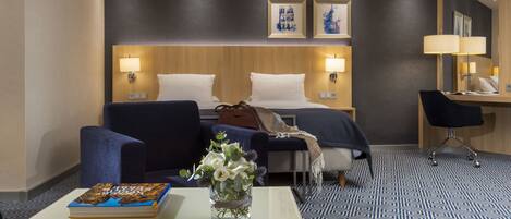 Una habitación de hotel con una cama, dos sillas, un escritorio y una mesa de centro. Hay un libro y un jarrón con flores sobre la mesa.