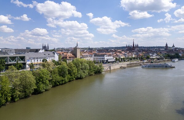 A river with a boat, buildings along the riverbank, and a distant city skyline.