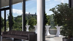 A modern interior with a leather sofa, large windows, and a view of a historic building. - Maritim Hotel Würzburg (Würzburg)