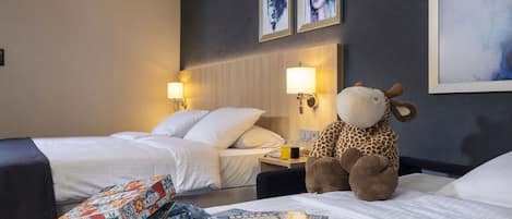 Habitación de hotel con dos camas, un peluche gigante de jirafa y un juego de mesa sobre la cama.