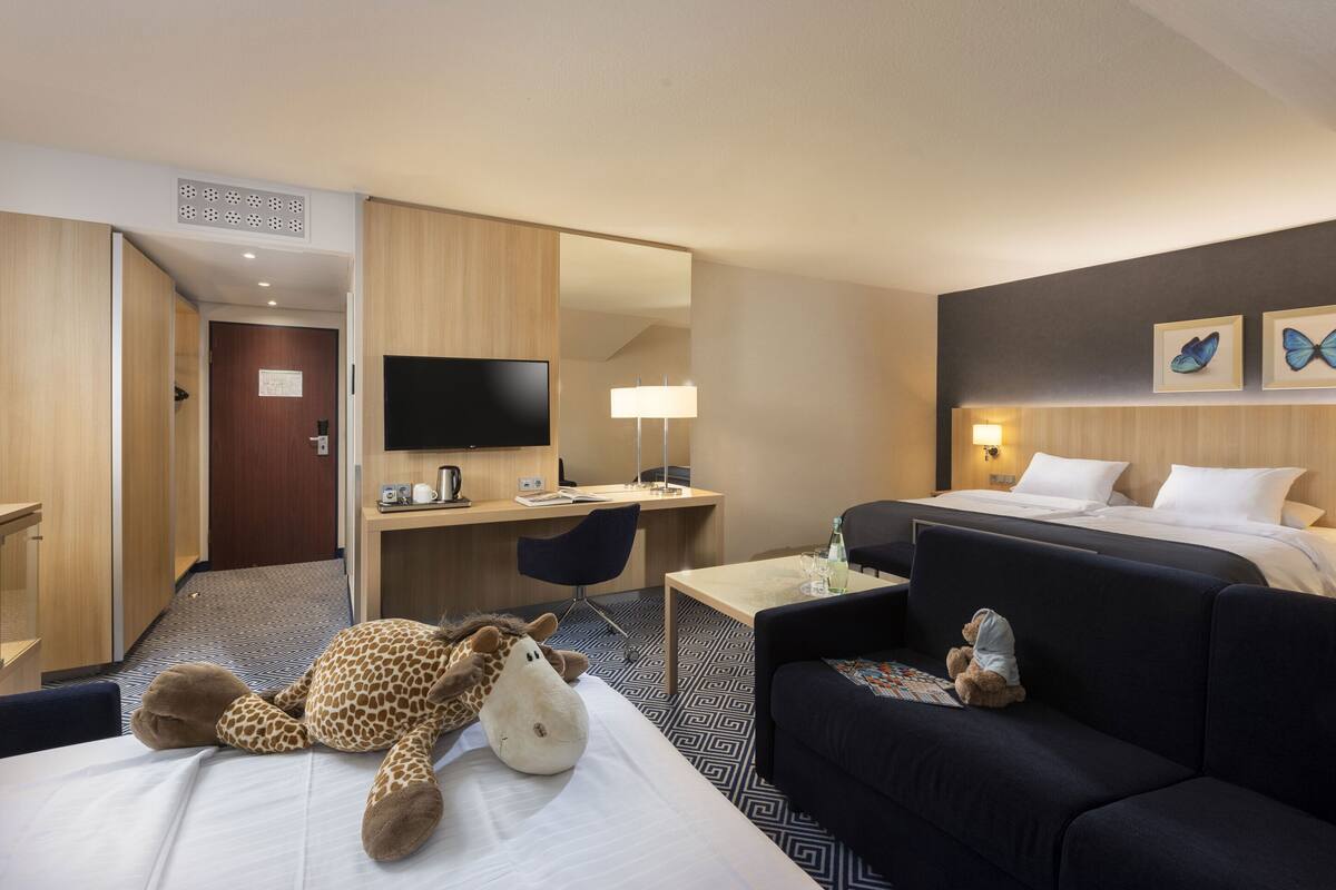A hotel room with a bed, a desk, a TV, a sofa, and a giraffe plush toy.