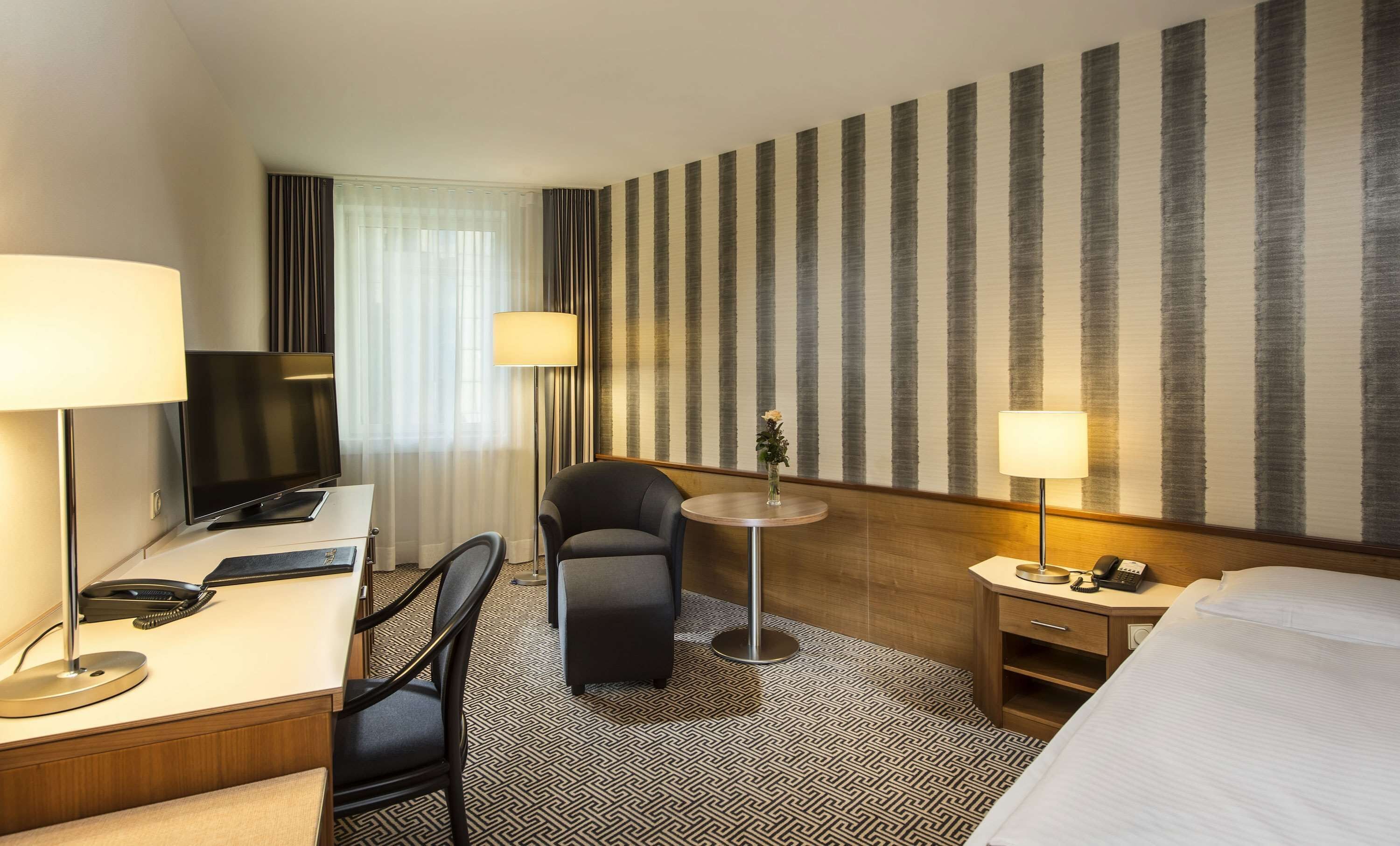 Een hotelkamer met een bureau, stoel, bed en een gestreepte wand.
