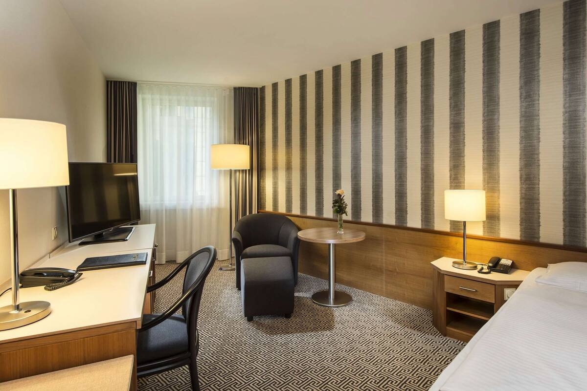 A hotel room with a desk, chair, bed, and a striped wall.