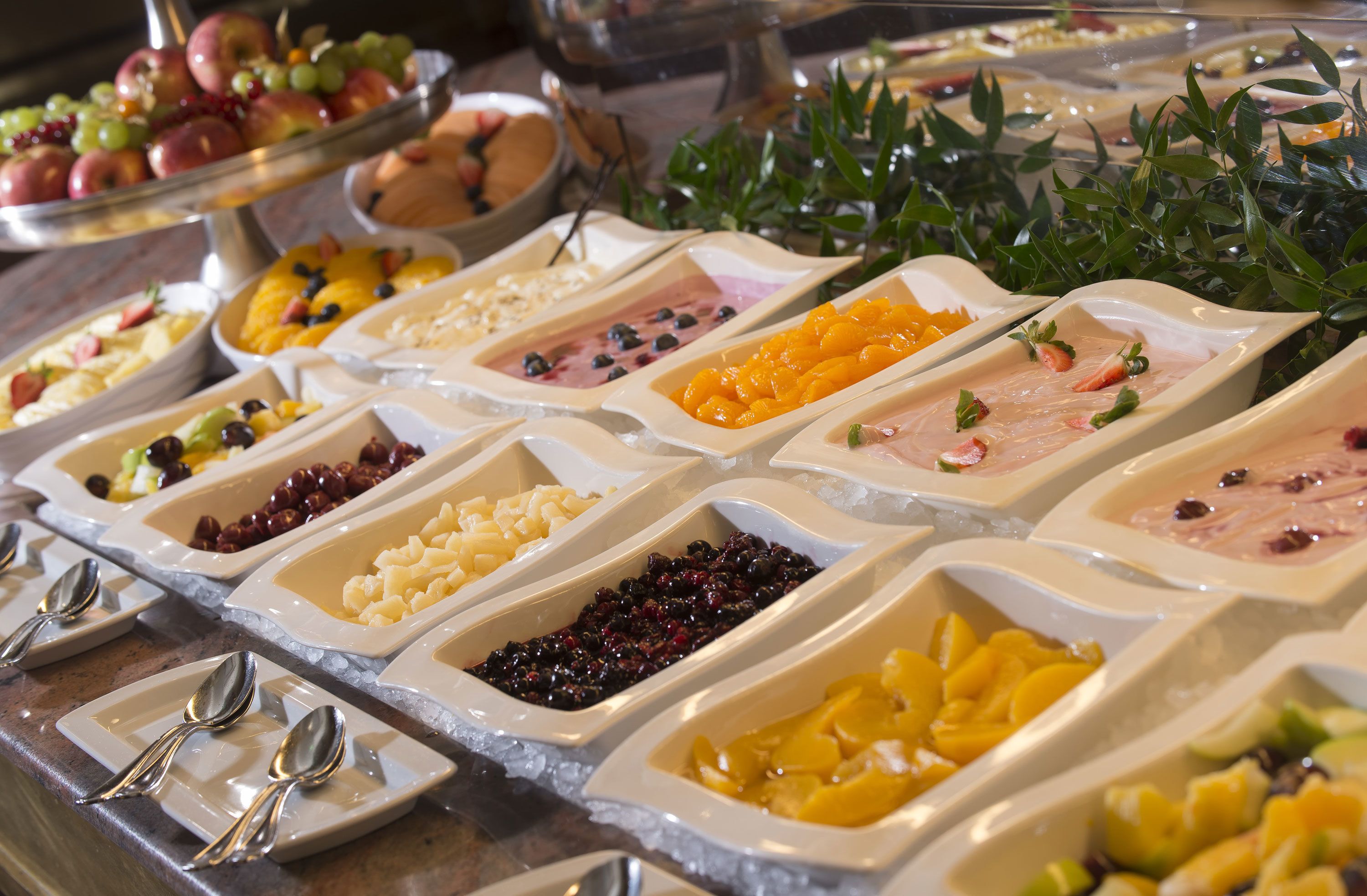 A buffet with various food options arranged in white trays on a table.