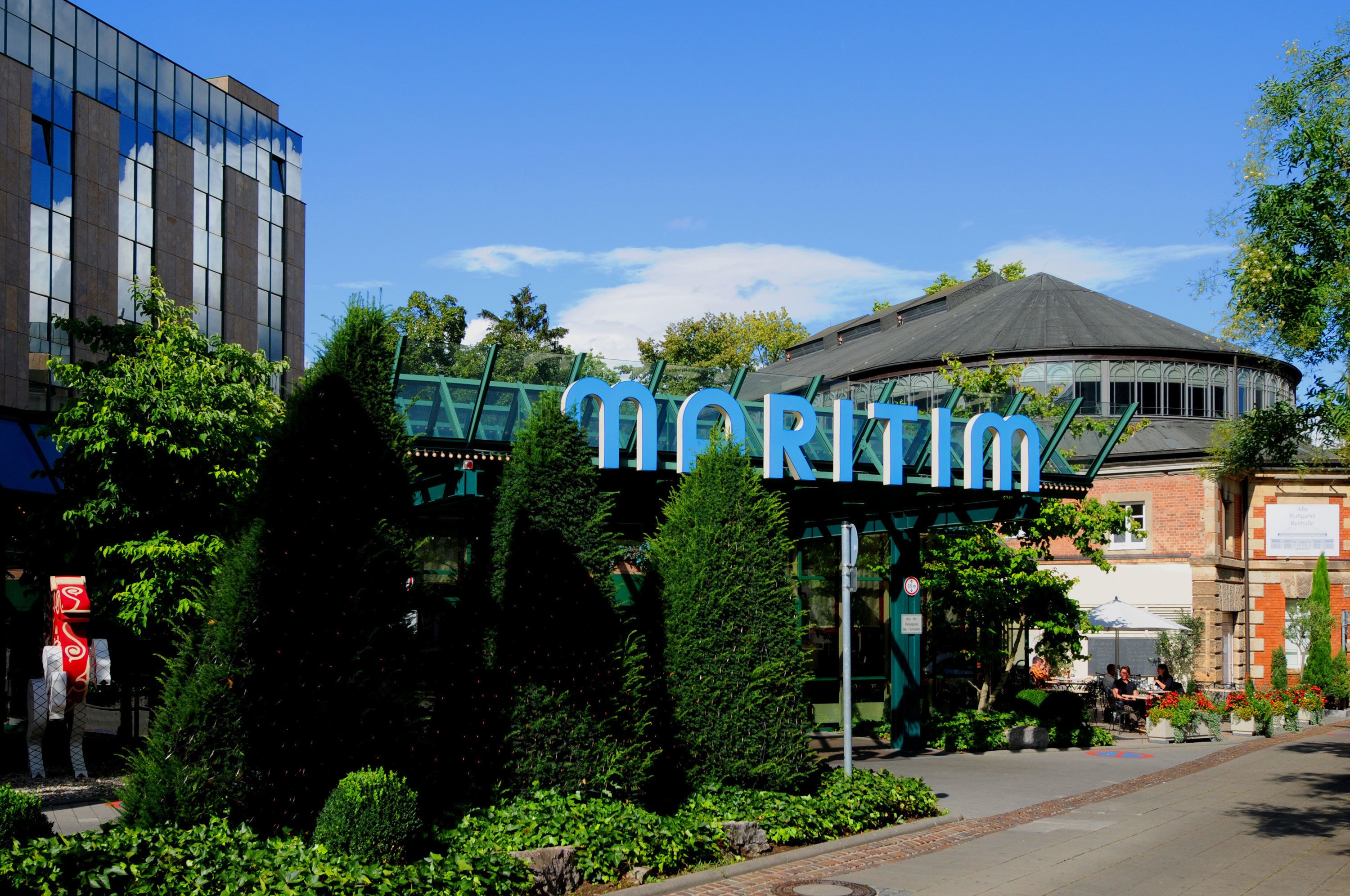 Un hotel con un llamativo letrero 'MORITZ', rodeado de vegetación y un edificio moderno.