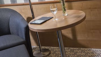 A hotel room with a round table, a vase with a single flower, a wine glass, and a tablet.