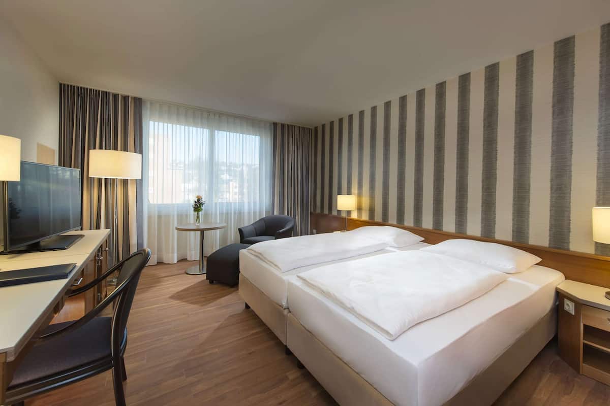 Hotellihuone, jossa on sänky, työpöytä, tuoli, televisio ja lamput.