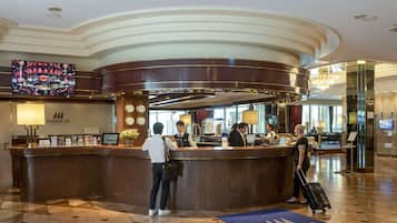 A hotel reception area with a curved counter, a television screen, and a clock.