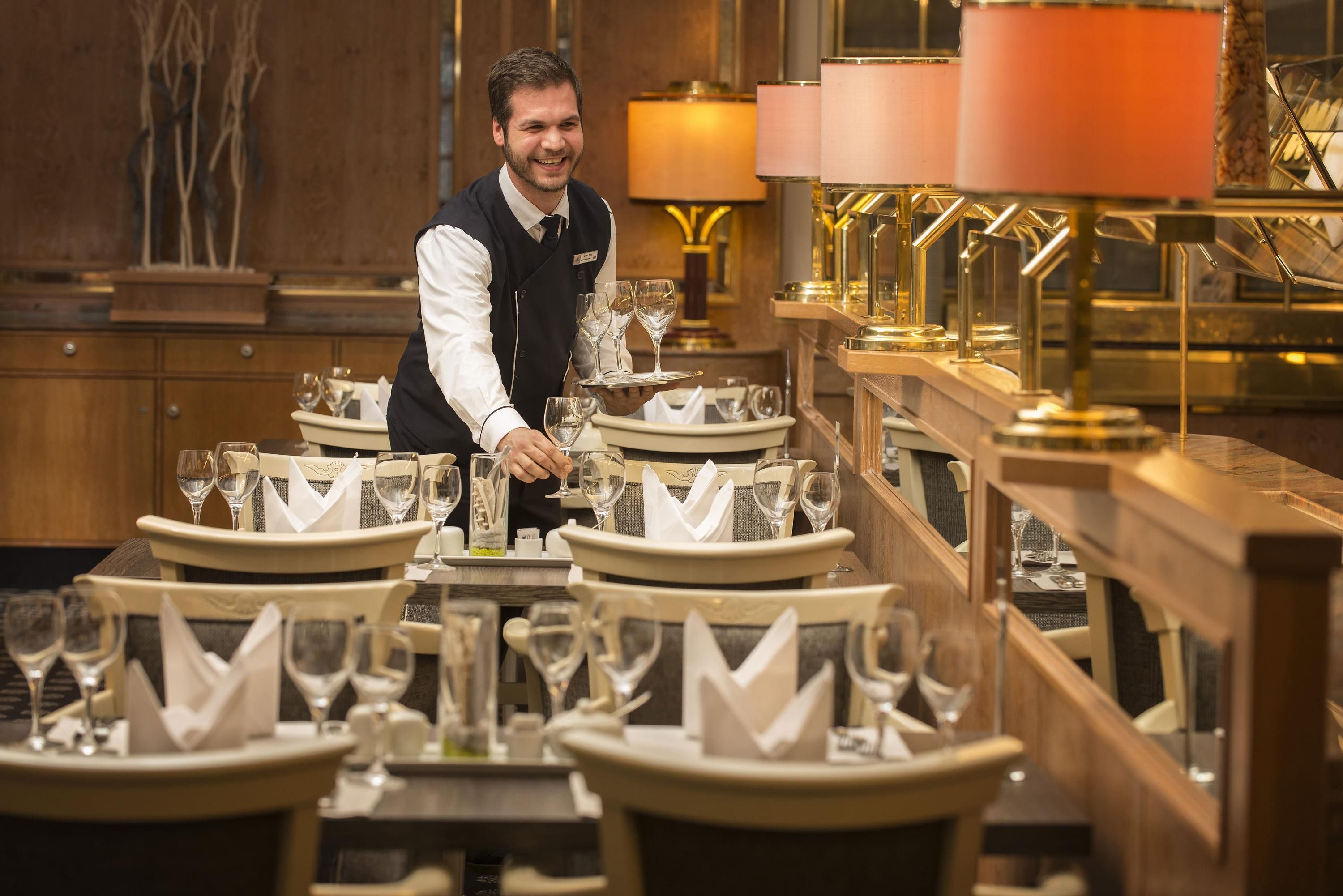Ein Kellner serviert Weingläser an einem Tisch in einem Restaurant mit warmer Atmosphäre und stilvoller Einrichtung.