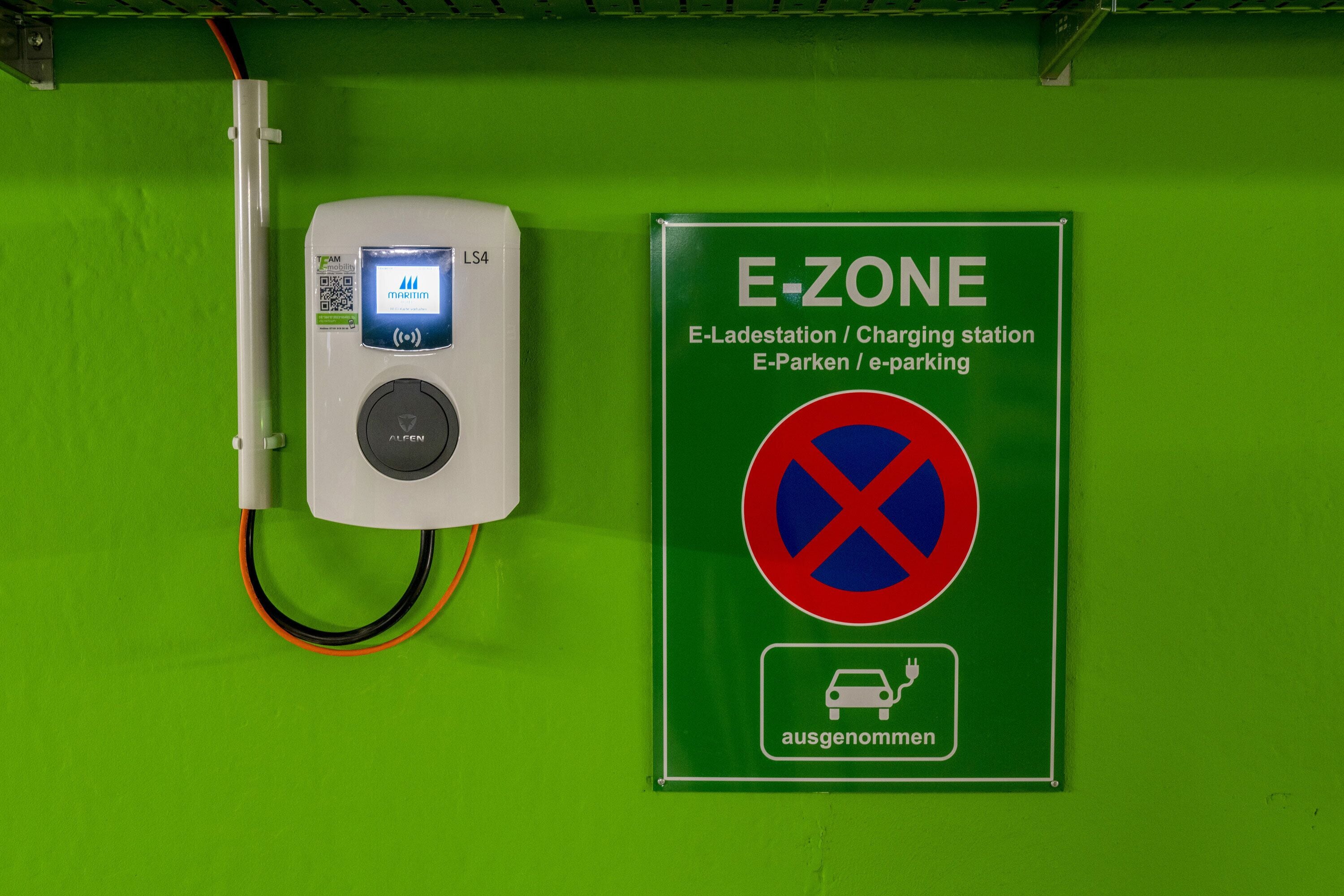 Une borne de recharge pour véhicules électriques, avec un panneau indiquant qu’il s’agit d’une borne de recharge E-ZONE.