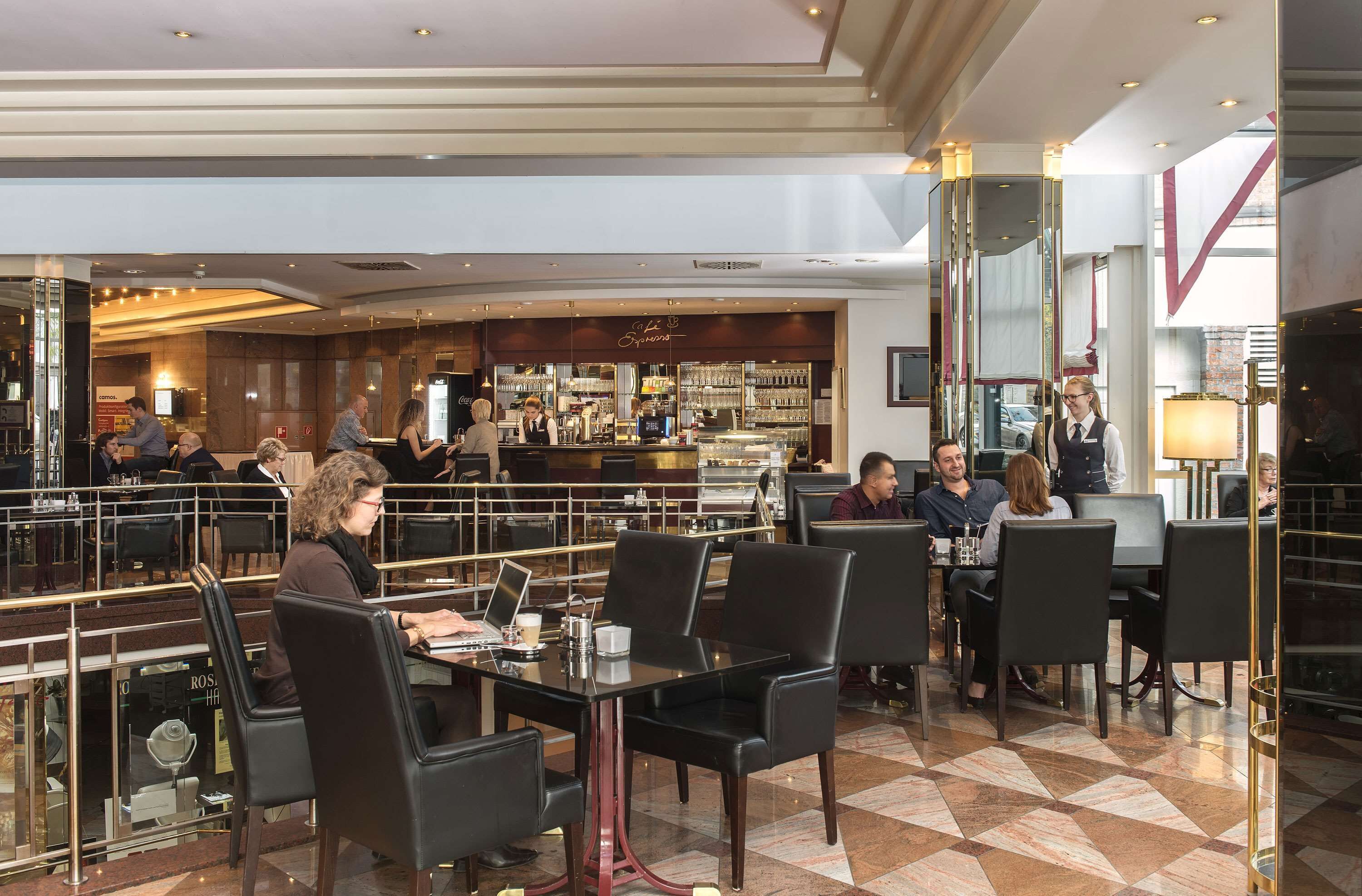 Un hall de hotel espacioso con varias zonas de estar, un bar y un restaurante visible al fondo.