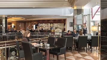 Un hall de hotel espacioso con varias zonas de estar, un bar y un restaurante visible al fondo.