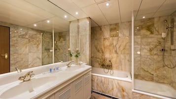 Un baño moderno con un lavamanos grande de mármol, una bañera y una ducha con mampara de vidrio.